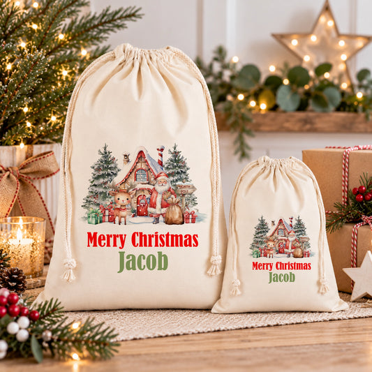 two Christmas-themed drawstring bags, one larger and one smaller, both with a festive illustration of Santa Claus and Christmas trees. The larger bag is labeled "Merry Christmas Jacob" and the smaller bag is labeled "Merry Christmas Jacob". The bags are placed on a table with holiday decorations, including a star and pine branches, creating a cozy and festive atmosphere.
