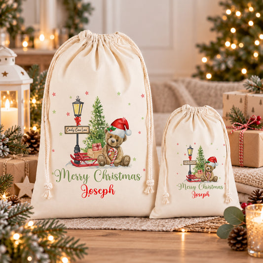 two white drawstring bags with Christmas-themed designs, including a teddy bear and a Christmas tree, placed on a wooden surface.