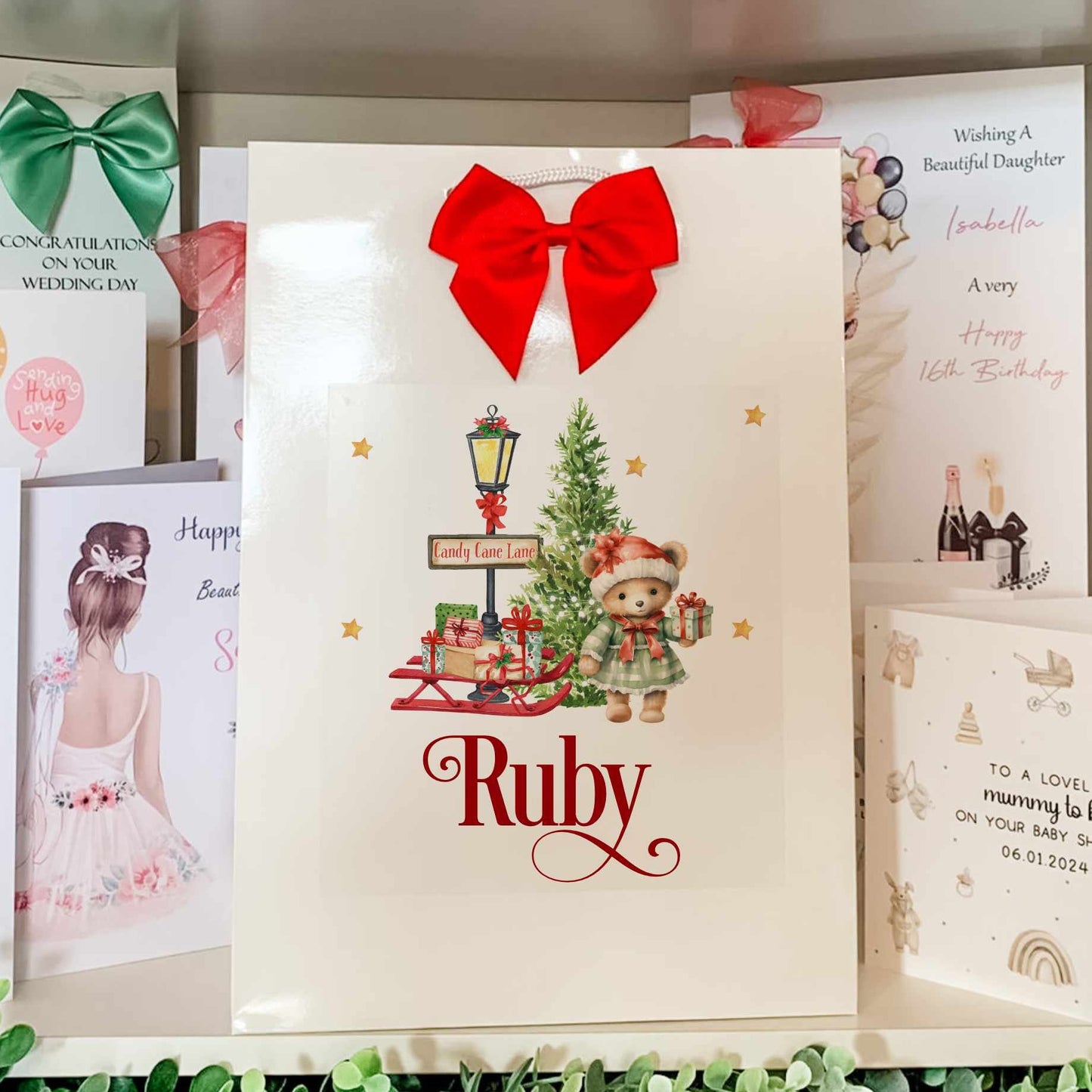 christmas gift bag for girl, with teddy bear next to christmas tree and sleigh of gifts.