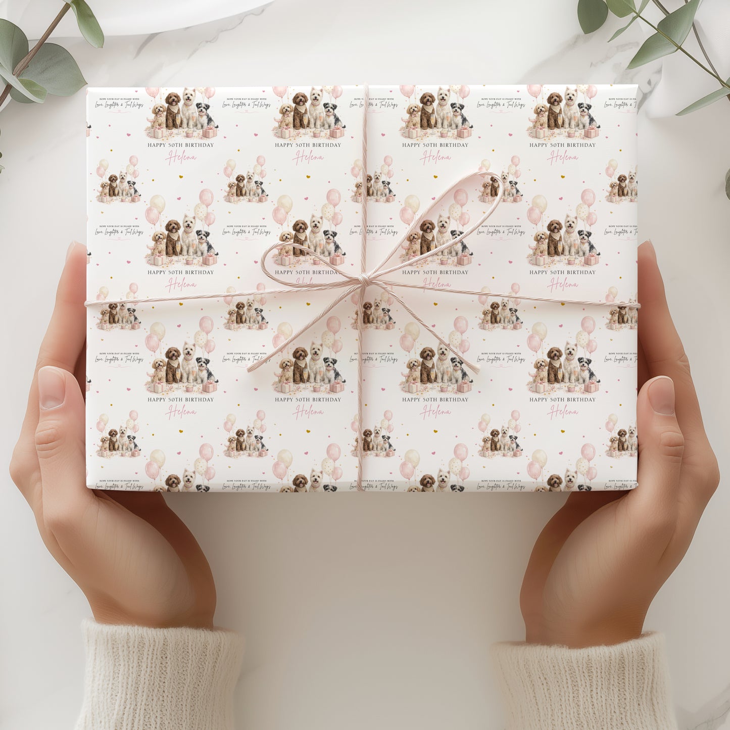 A pair of hands holding a gift box with a pattern of dogs and balloons on the wrapping paper.