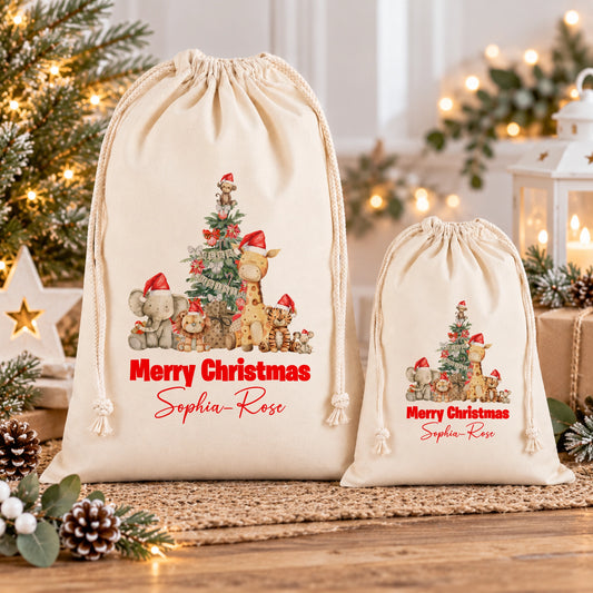 Two white drawstring bags with Christmas-themed illustrations and personalized messages are displayed on a wooden surface, surrounded by holiday decorations and pine cones.