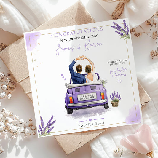 A personalized wedding congratulations card featuring an illustration of a couple in a purple van, styled on top of kraft envelopes and white fabric with dried flowers.