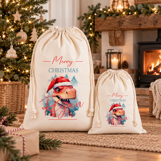 Two white drawstring bags with Christmas-themed designs, featuring a dinosaur wearing a Santa hat and the text "Merry Christmas" printed on them.
