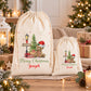 two white drawstring bags with Christmas-themed designs, including a teddy bear and a Christmas tree, placed on a wooden surface.