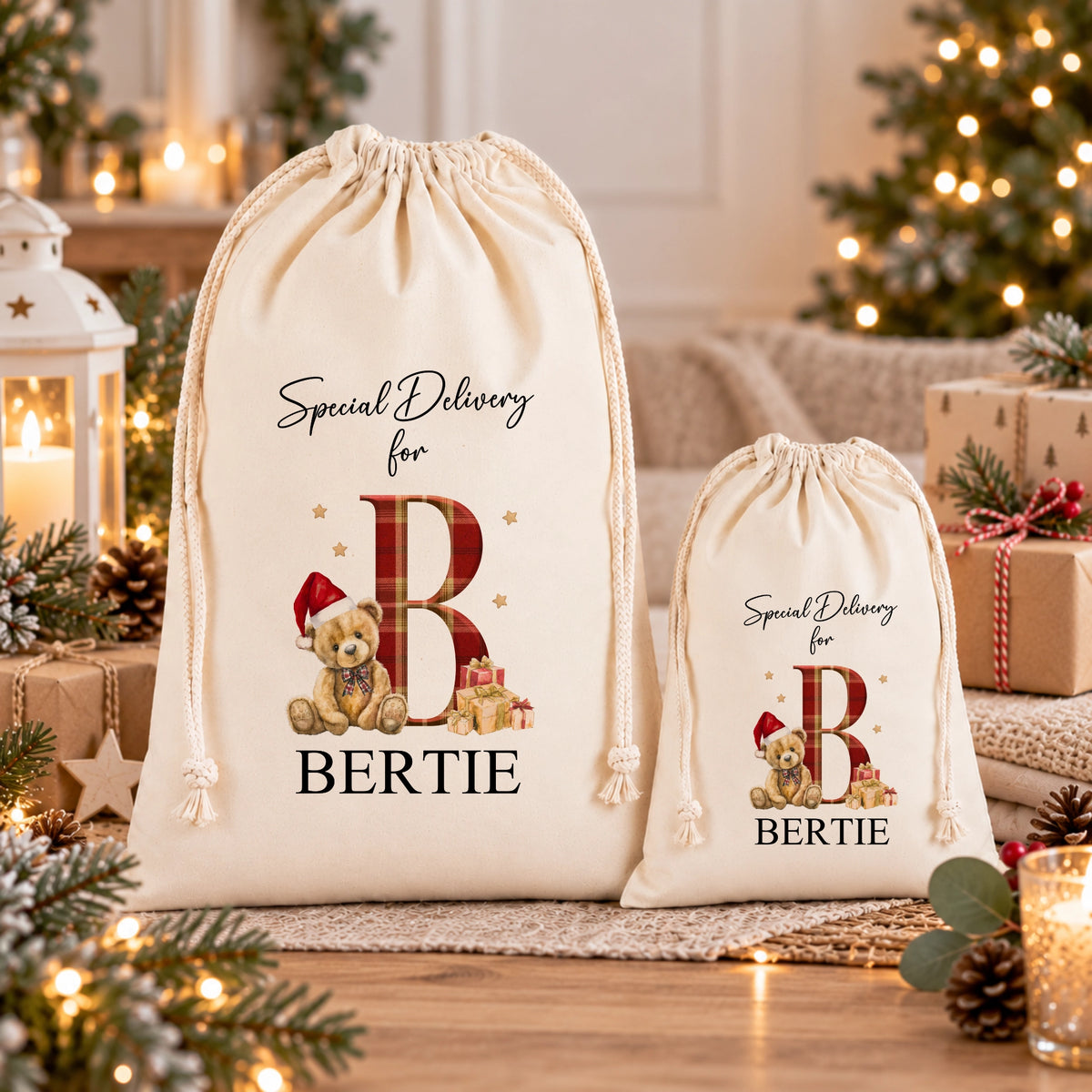 two white drawstring bags with a teddy bear design and the letter "B" printed on them, placed on a table with Christmas decorations and gifts.