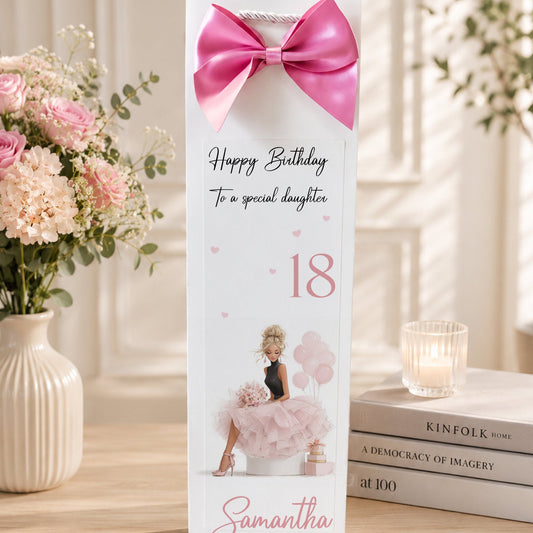 Gift box with pink bow and birthday message on a decorative table with flowers and books.