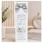A personalized silver-toned champagne bottle gift tag with a matching satin bow, featuring a custom 'Happy Silver Wedding Anniversary' message for Andrew & Lois. The tag is styled on a tabletop next to a vase of baby's breath and a stack of books.