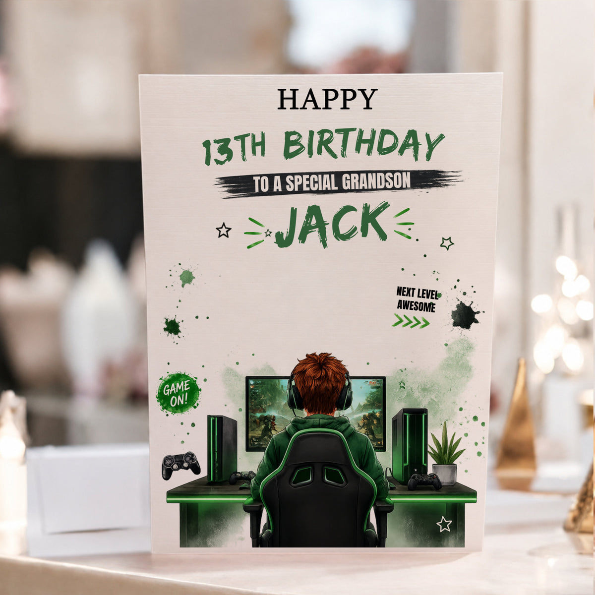 A personalized gaming-themed 13th birthday card for a special grandson, featuring an illustration of a gamer sitting at a desk with a computer setup. The card is displayed upright on a table with a blurred indoor background.