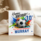A square birthday card with a soccer ball graphic and colorful paint splashes, reading 'Happy Birthday! any age any name and relationship displayed on a light surface with draped fabric in the background.