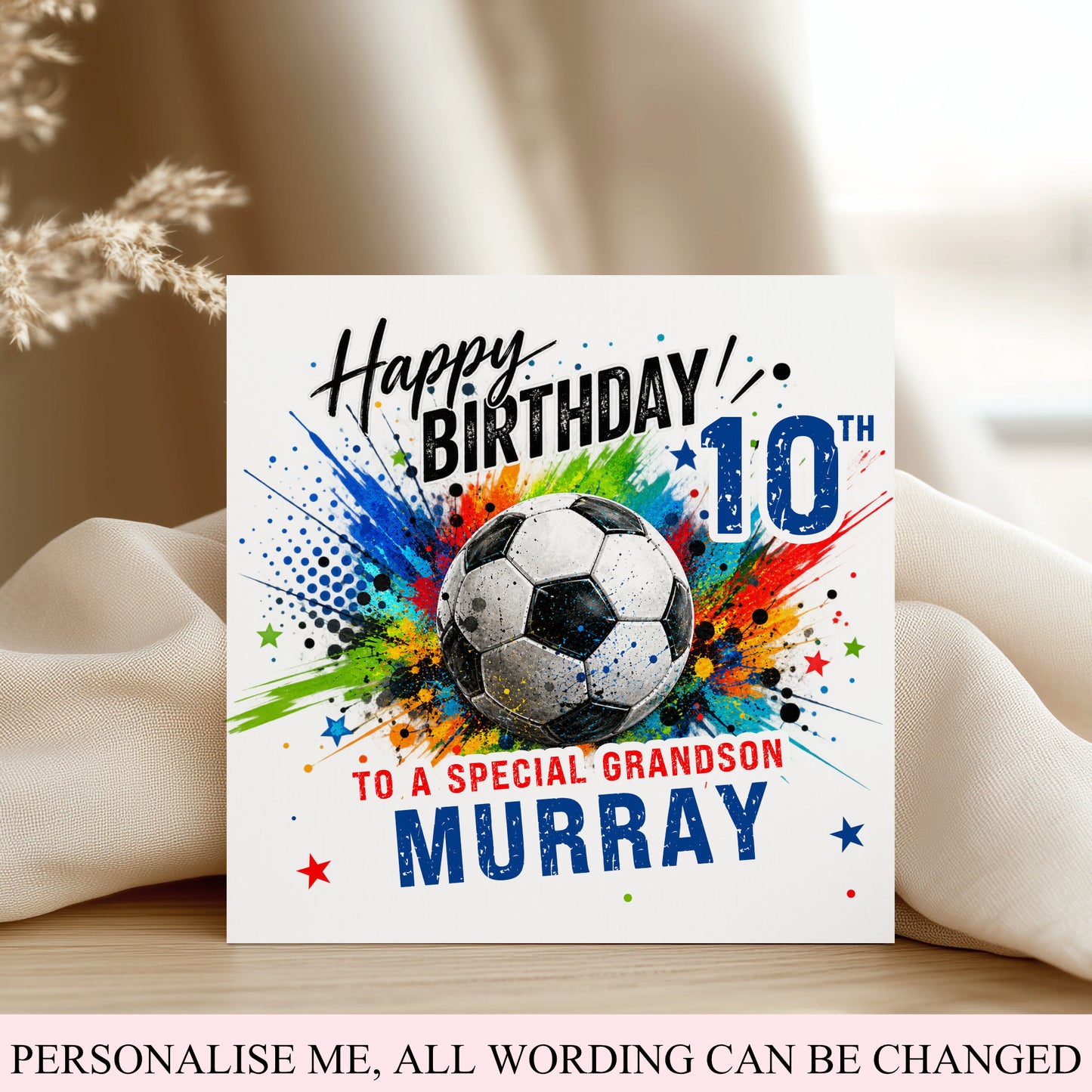 A personalized 10th birthday card for a soccer fan, featuring a soccer ball graphic surrounded by colorful paint splatters and the text any age any relationship any name'. The card is displayed on a wooden surface with draped beige fabric in the background.