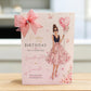 A pink birthday card addressed to a special granddaughter, featuring an illustration of a woman in a floral pink dress holding a heart-shaped balloon with the number 50. The card is decorated with a large pink bow and stands on a light wooden surface.