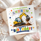 A square birthday card for a grandson, featuring a cartoon excavator digging dirt and the text 'TO AN AMAZING GRANDSON ANDREW HAPPY BIRTHDAY! HAVE AN AMAZING DAY!'. The card is styled on top of kraft paper envelopes and white fabric with dried flowers.