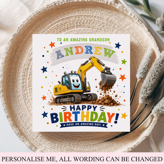 A personalized birthday card for a grandson, featuring a cartoon yellow excavator digging up dirt, with the text 'TO AN AMAZING GRANDSON ANDREW HAPPY BIRTHDAY! HAVE AN AMAZING DAY!'. The card is displayed on a woven straw hat with a pink fabric background.