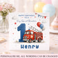 A square birthday card for a grandson's first birthday, featuring a red fire truck, a large blue number 1, balloons, stars, and the text 'HAPPY BIRTHDAY TO A Very Special Grandson' and 'Henry'. The card is displayed on a decorated party table with balloons and flowers in the background.