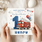 A personalized first birthday card for a grandson, held by two hands. The card features a red fire truck, a large blue number 1, balloons, and the text 'HAPPY BIRTHDAY TO A Very Special Grandson' and 'Henry'.