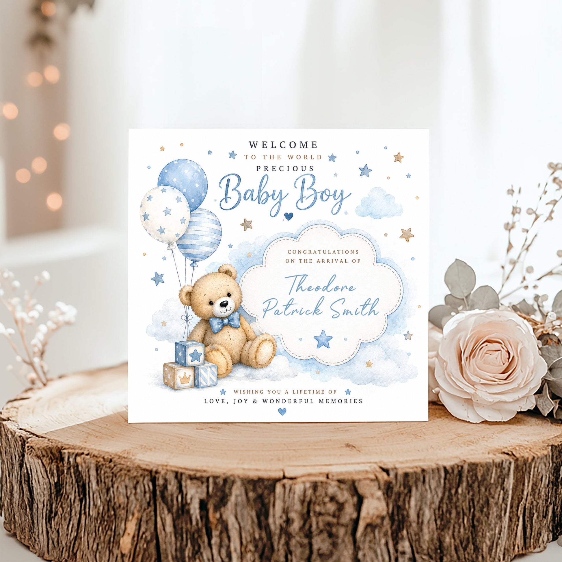 A personalized baby shower announcement card for a boy, styled on a rustic wood slice with a pink rose and dried flowers. The card features a watercolor illustration of a teddy bear with balloons and stars in blue and white.