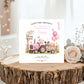 A personalized first birthday card for a granddaughter, featuring a pink cartoon tractor and pig illustration, displayed on a rustic wood slice with a rose and dried flowers.