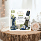 A personalized golf-themed 60th birthday card displayed on a rustic wood slice with decorative flowers. The card features a golf course illustration, a golfer, a golf bag with clubs, a cap, a golf ball, and text reading 'Happy Birthday to you John Have an Amazing Day' along with '60'.