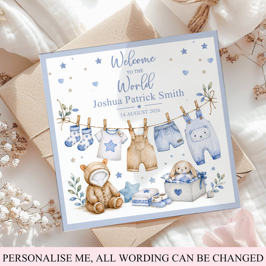 A personalized baby boy's first birthday card styled on top of kraft paper envelopes and white fabric. The card features watercolor illustrations of baby clothing, a teddy bear, and a baby carriage, with the text 'Welcome to the World Joshua Patrick Smith 14 August 2026'.