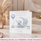 A personalized baby shower congratulations card featuring a watercolor illustration of a baby elephant on a crescent moon with blue flowers and balloons. The card is displayed on a marble tabletop with decorative dried grass, a candle, and books in the background.