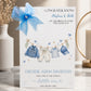 A white new baby boy greeting card displayed upright in a softly styled neutral setting. The card features a blue denim baby jacket, cream trousers, a blue and white striped top and a matching blue baby cap hanging from a decorative clothesline. Blue hearts, gold stars and delicate botanical details surround the clothing.