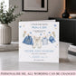 A personalized baby shower congratulations card displayed on a tabletop in a styled home interior. The card features watercolor illustrations of baby clothing hanging on a clothesline, with customizable text for a boy and girl.