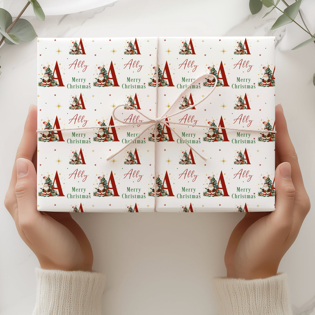 Personalised Christmas wrapping paper featuring Santa Claus, Christmas tree, large initial and name in red, green, gold and white festive design.