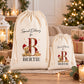 two white drawstring bags with a teddy bear design and the letter "B" printed on them, placed on a table with Christmas decorations and gifts.