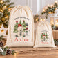 two white drawstring bags with Christmas-themed illustrations and text, placed on a wooden surface.