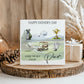 A greeting card with golf-related illustrations and text, placed on a wooden surface with a gift box and pine cone nearby.