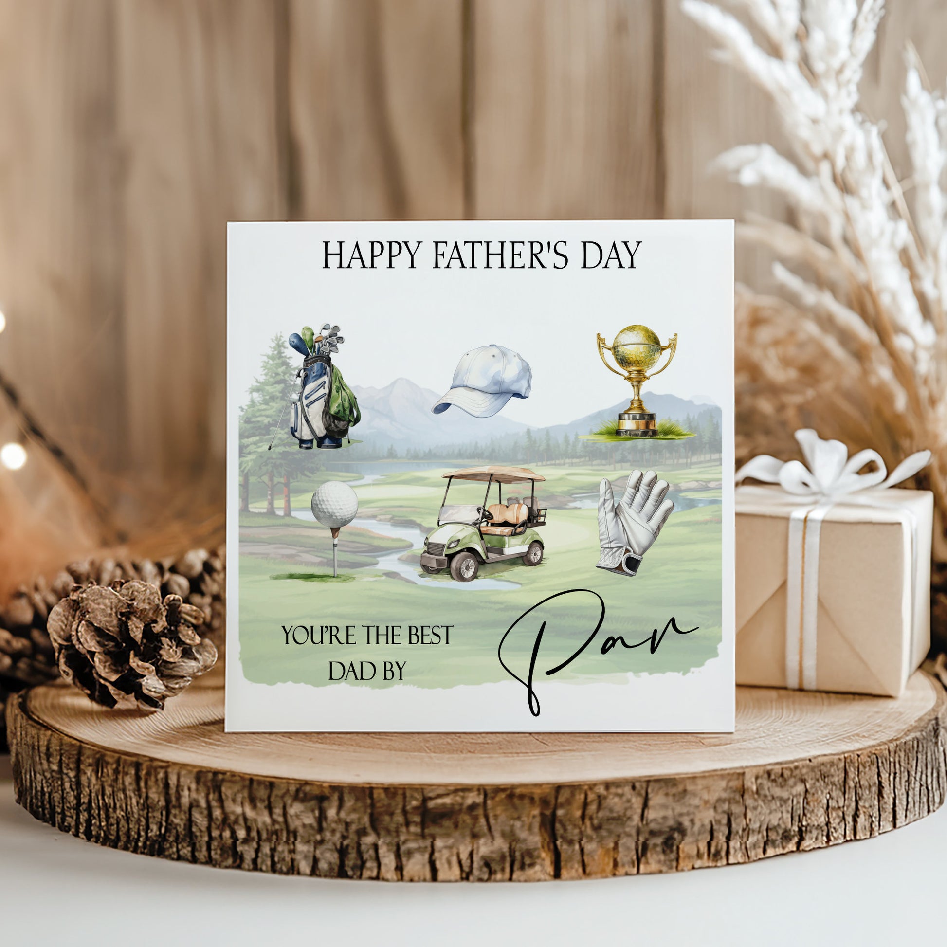 A greeting card with golf-related illustrations and text, placed on a wooden surface with a gift box and pine cone nearby.