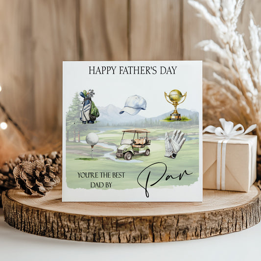 A greeting card with golf-related illustrations and text, placed on a wooden surface with a gift box and pine cone nearby.