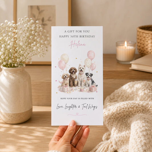 A hand holding a birthday card with a picture of four dogs and balloons, along with a message about a birthday gift.