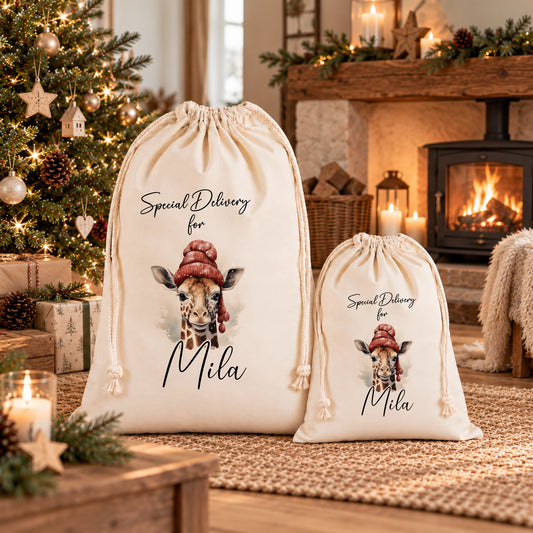 Two white drawstring bags with a giraffe design, placed in front of a Christmas tree and a fireplace.