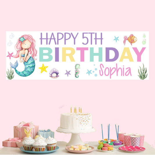 a birthday banner with a mermaid sitting on top of a table