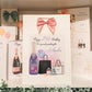 a birthday card with a pink bow and a bottle of champagne