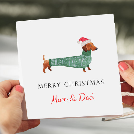 a woman holding a christmas card with a dachshund in a sweater